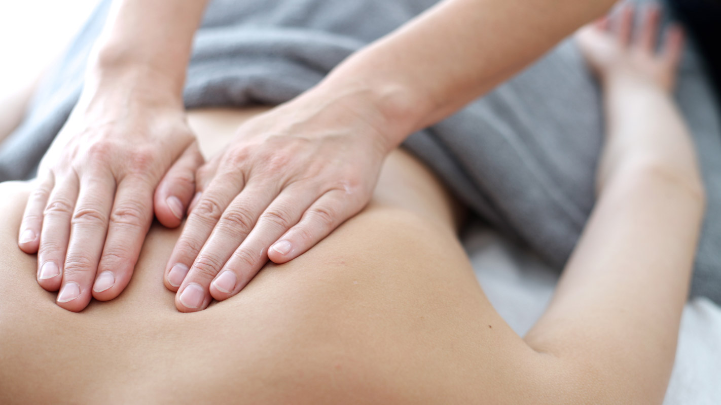 Hands massaging and easing back pains while person is on a table.
