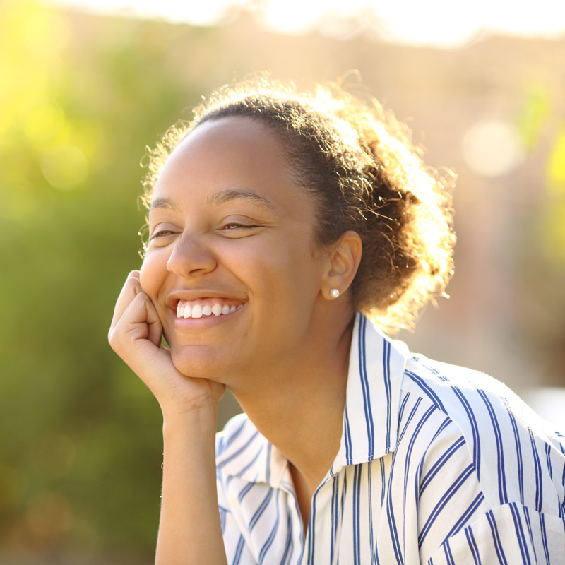 Woman outside smiling, thinking, and relaxed. 